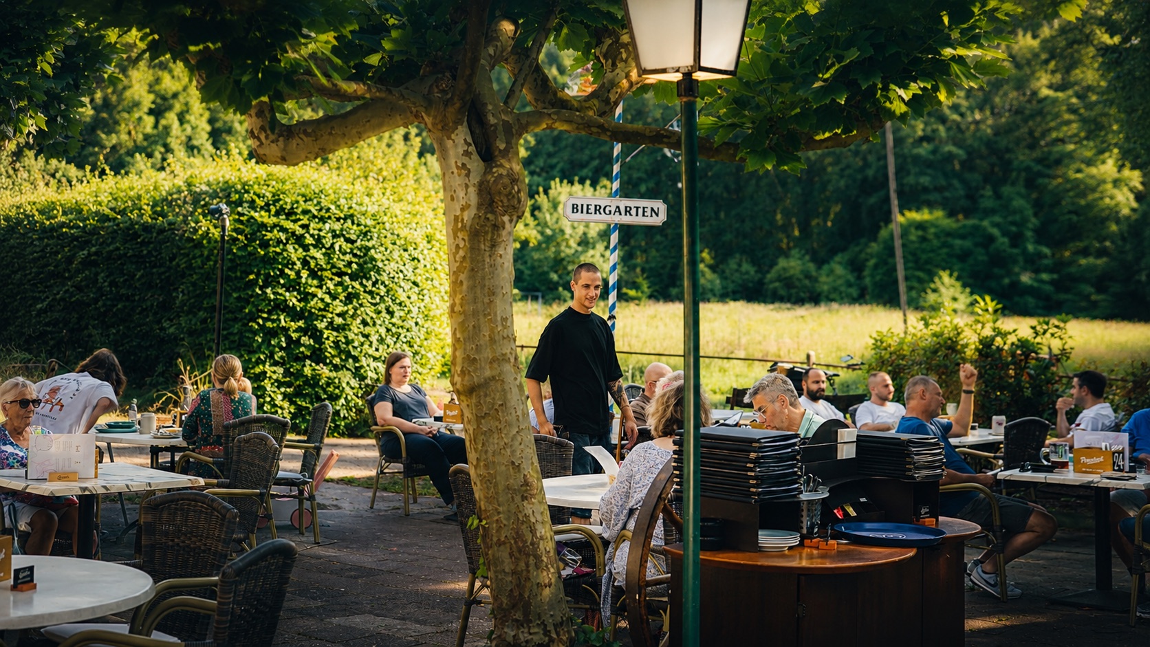 Waldfrieden Biergarten Viersen — Gäste und Kellner unter alten Bäumen in der Abendsonne